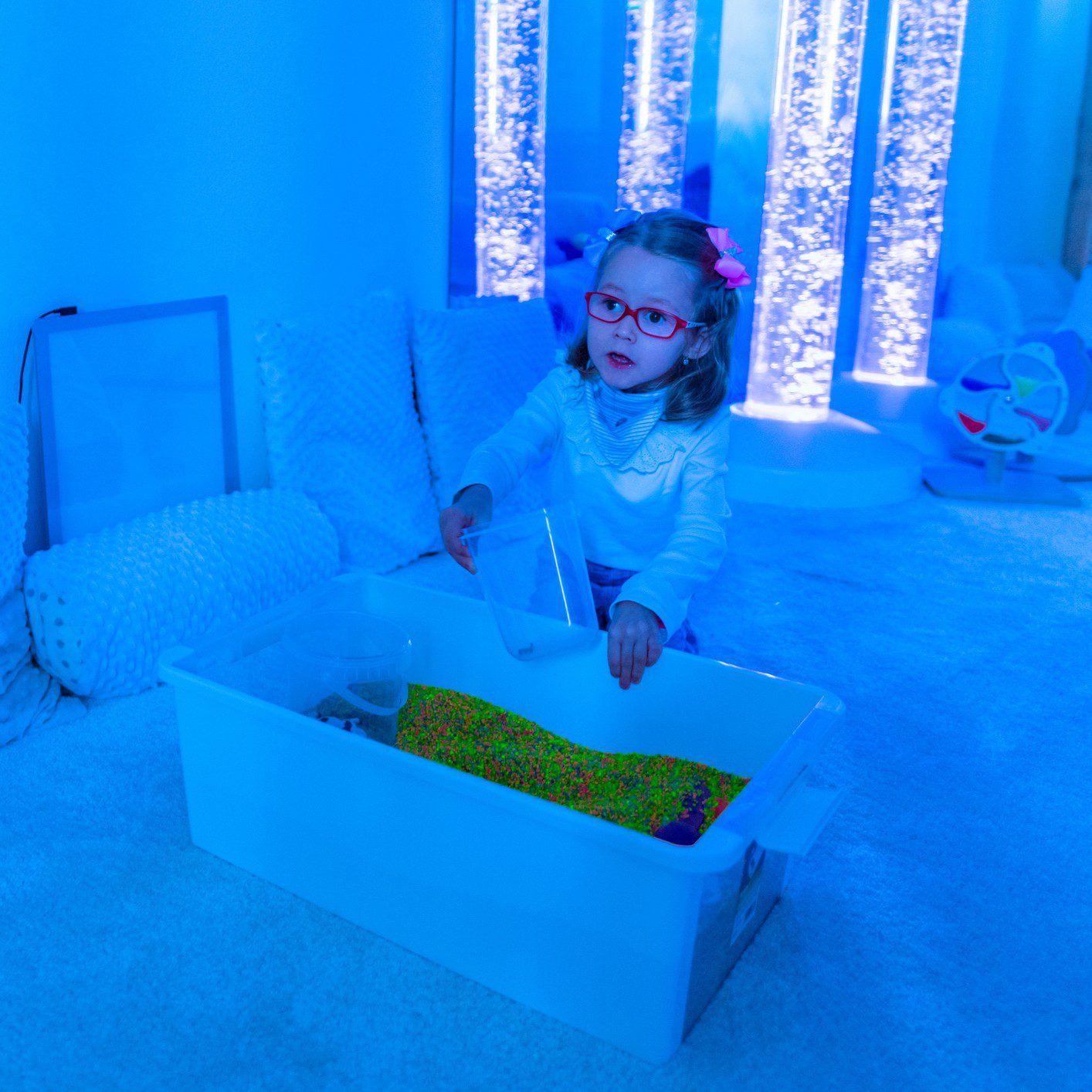 Child playing sensory bin near bubble tube lights