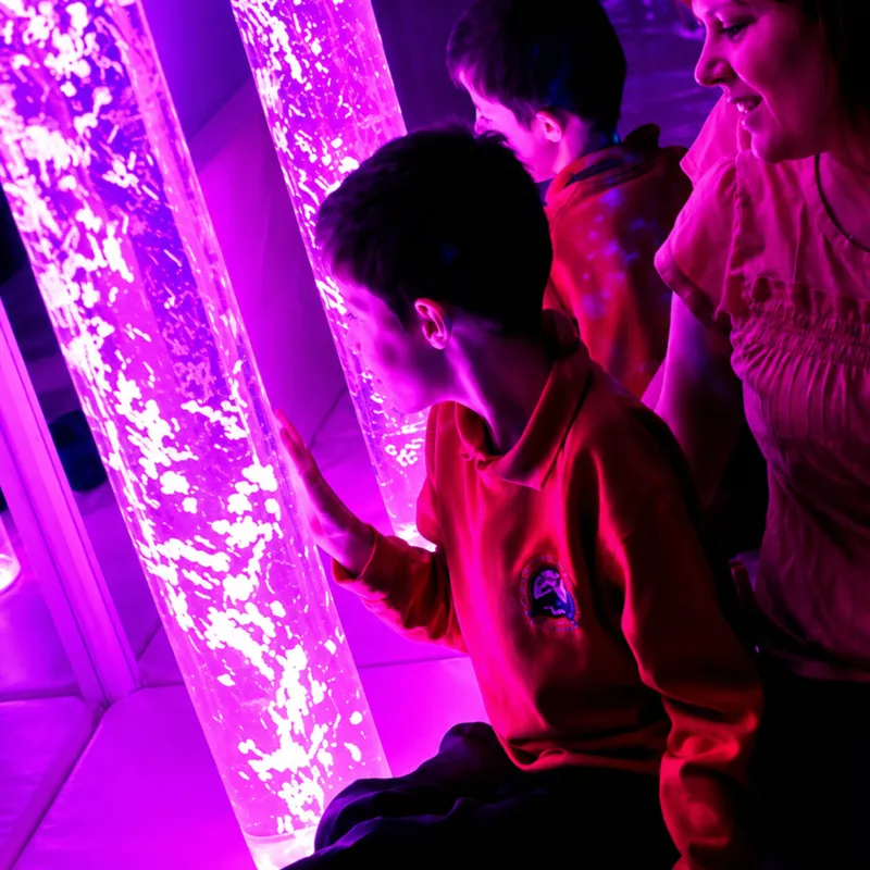 Children exploring illuminated purple bubble tube exhibit